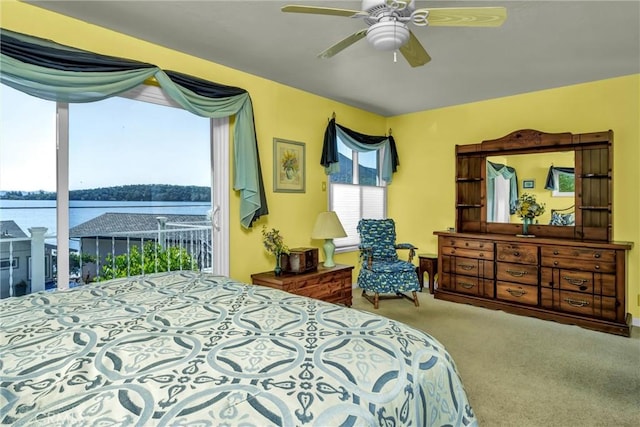 carpeted bedroom with a water view, access to outside, and a ceiling fan