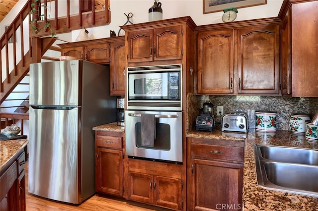 36575 Mudge Ranch Rd, Coarsegold, CA 93614 - kitchen featuring appliances with stainless steel finishes, dark stone countertops, light wood-style flooring, decorative backsplash, and a sink