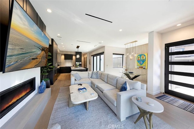 living room featuring baseboards, a glass covered fireplace, light wood-style floors, and recessed lighting