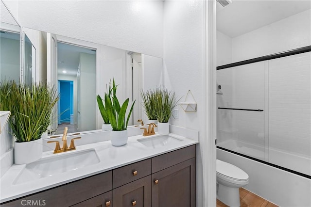 bathroom featuring toilet, wood finished floors, double vanity, and shower / bath combination with glass door
