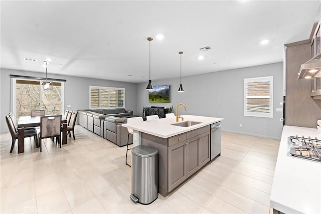kitchen featuring a sink, appliances with stainless steel finishes, light countertops, a kitchen island with sink, and pendant lighting