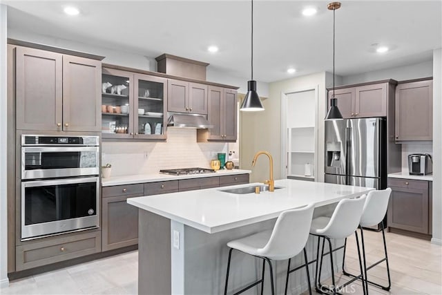 21123 Mill Valley Ct, Riverside, CA 92507 - kitchen featuring stainless steel appliances, under cabinet range hood, tasteful backsplash, an island with sink, and light countertops