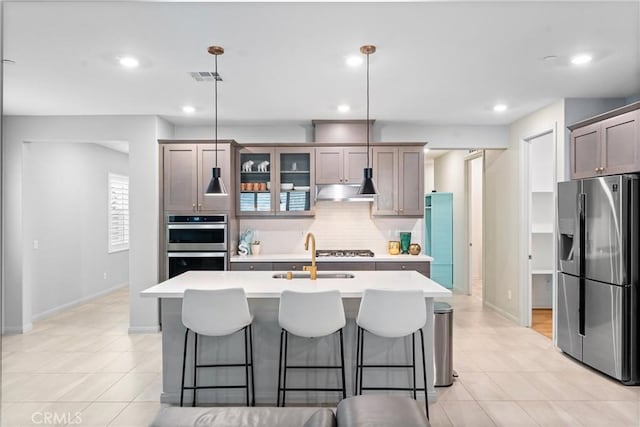 kitchen with appliances with stainless steel finishes, a sink, tasteful backsplash, light countertops, and a breakfast bar area