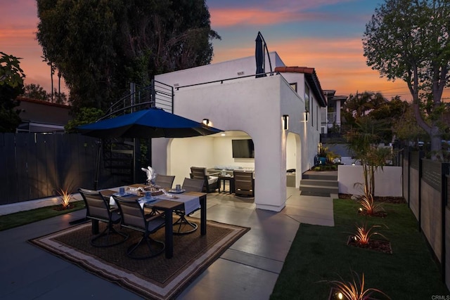 back of property at dusk featuring outdoor dining area, a patio area, and stucco siding