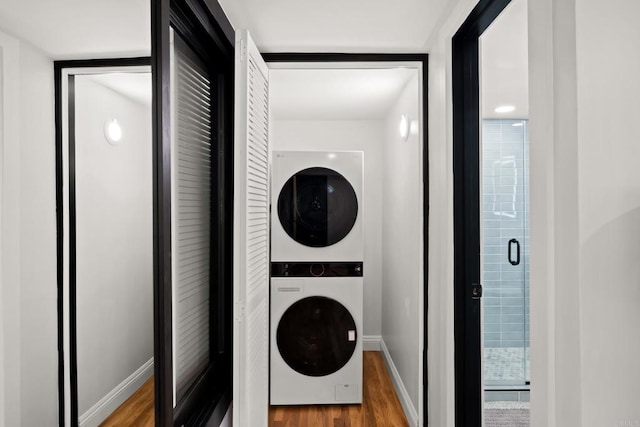 washroom featuring stacked washer and clothes dryer, wood finished floors, and baseboards