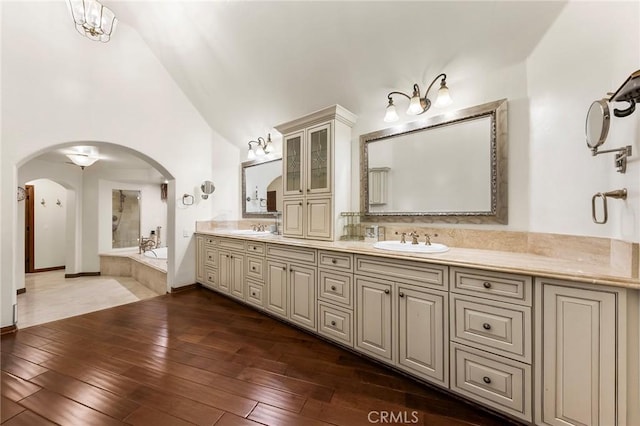 bathroom with a sink, a bath, vaulted ceiling, and hardwood / wood-style floors
