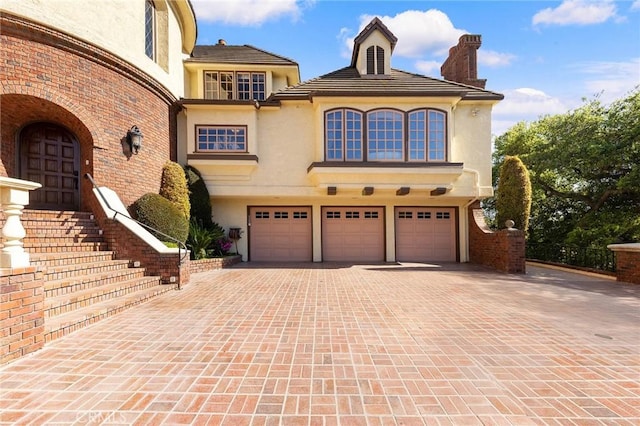 mediterranean / spanish house featuring a garage, stucco siding, a chimney, and driveway