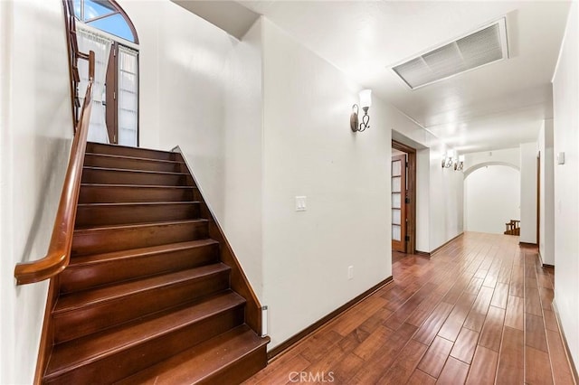stairway with arched walkways, baseboards, wood finished floors, and visible vents