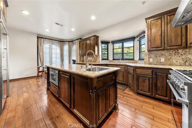 kitchen with ventilation hood, a sink, high end stove, backsplash, and visible vents