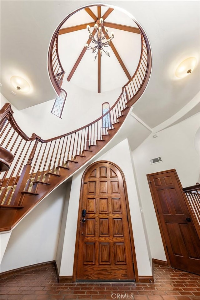 foyer entrance with stairway, baseboards, visible vents, and a towering ceiling