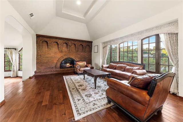living area featuring visible vents, a fireplace, high vaulted ceiling, dark wood-type flooring, and a tray ceiling