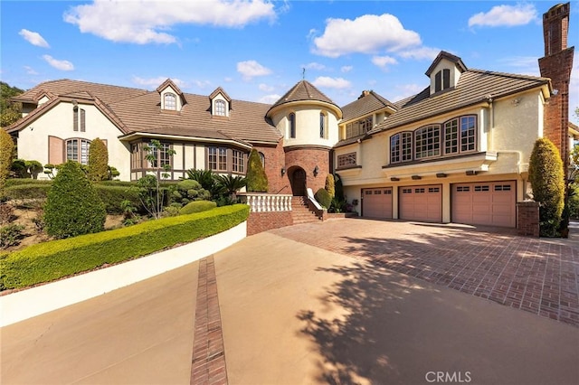 view of front facade with decorative driveway, an attached garage, a chimney, and stucco siding