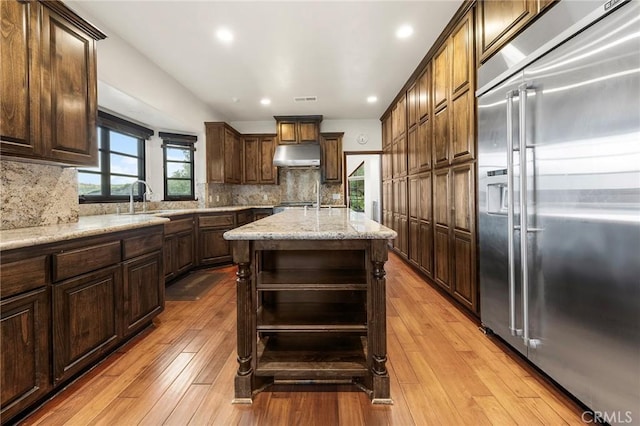 kitchen featuring open shelves, light wood-type flooring, built in refrigerator, under cabinet range hood, and a sink