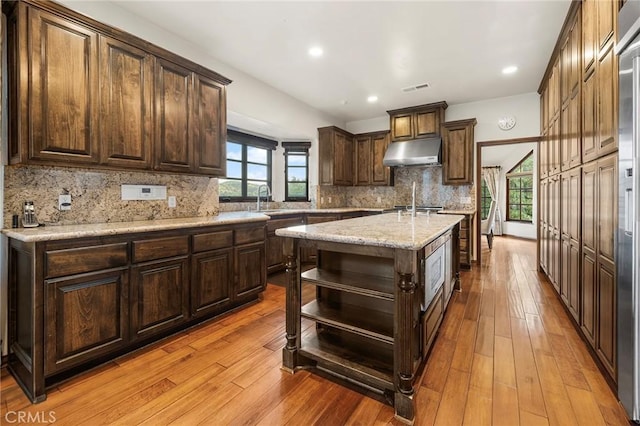 kitchen with visible vents, open shelves, a kitchen island with sink, dark brown cabinets, and under cabinet range hood