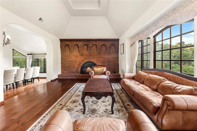living area with visible vents, a brick fireplace, lofted ceiling, and wood finished floors