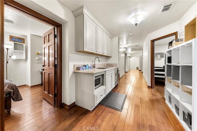 kitchen with a sink, light countertops, light wood-style flooring, stainless steel microwave, and visible vents