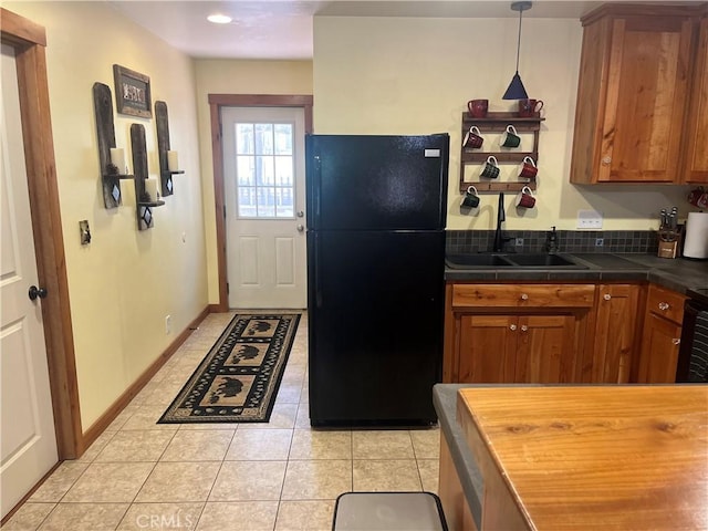kitchen with hanging light fixtures, a sink, freestanding refrigerator, brown cabinets, and light tile patterned flooring
