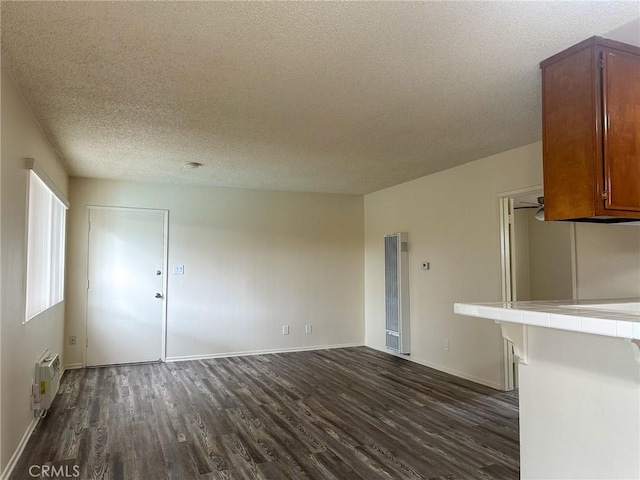 unfurnished living room with a textured ceiling, baseboards, and dark wood finished floors