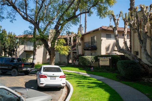 view of front of home featuring a tiled roof, uncovered parking, stucco siding, a front lawn, and a chimney
