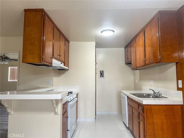 kitchen with baseboards, dishwasher, a sink, brown cabinets, and tile countertops