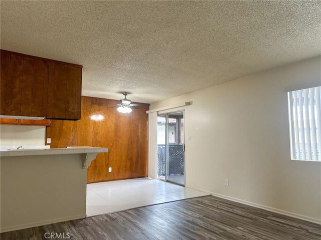 unfurnished living room featuring baseboards, a textured ceiling, a ceiling fan, wood walls, and wood finished floors
