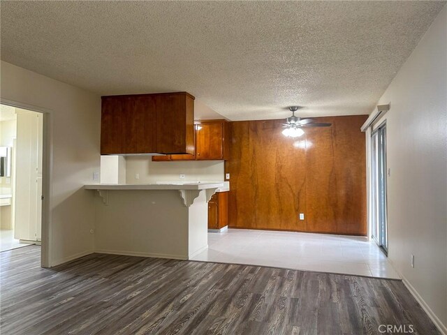 kitchen with light wood-type flooring, a peninsula, a ceiling fan, brown cabinetry, and a breakfast bar area