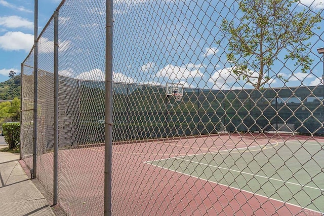 view of tennis court featuring community basketball court and fence