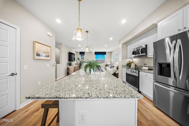 kitchen featuring light wood-style flooring, a kitchen island, white cabinets, stainless steel appliances, and pendant lighting