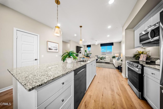 kitchen featuring open floor plan, a kitchen island with sink, light wood-style floors, appliances with stainless steel finishes, and a sink