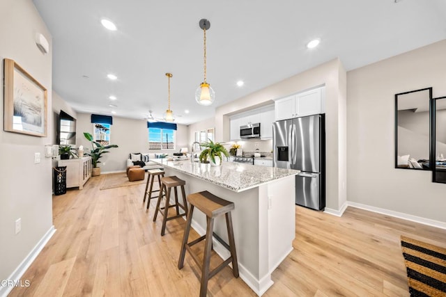 kitchen featuring light stone countertops, a kitchen bar, white cabinetry, appliances with stainless steel finishes, and a center island with sink