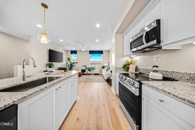 kitchen with a sink, stainless steel microwave, white cabinetry, and range with electric cooktop
