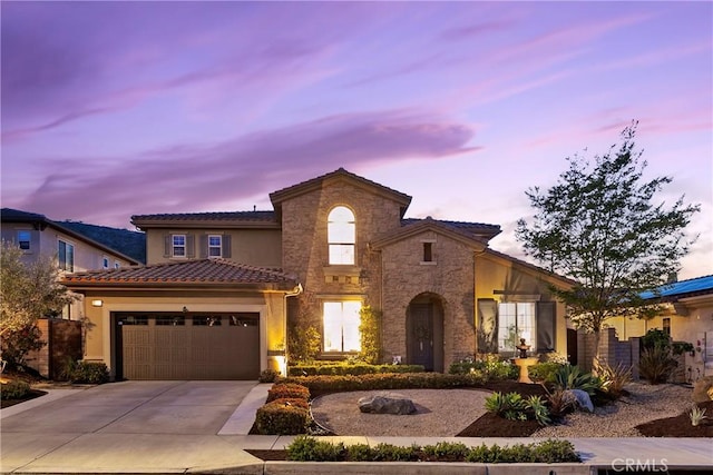 mediterranean / spanish home featuring driveway, stone siding, a tiled roof, a garage, and stucco siding