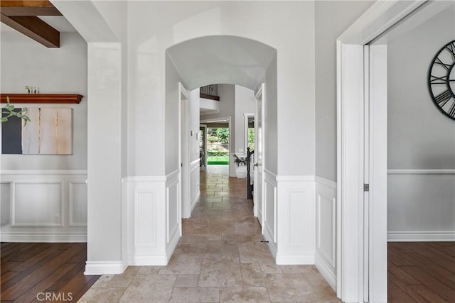 hallway with arched walkways, a decorative wall, and wainscoting