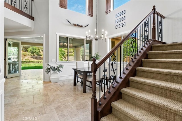 staircase with plenty of natural light, a chandelier, stone tile floors, and a towering ceiling