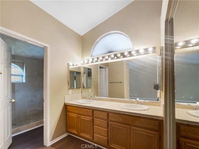 bathroom with double vanity, a sink, vaulted ceiling, and wood finished floors