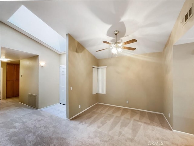 empty room featuring vaulted ceiling with skylight, a ceiling fan, visible vents, baseboards, and carpet floors