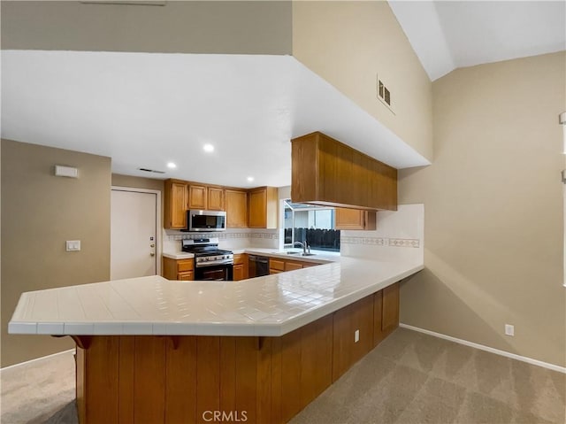 kitchen with light colored carpet, brown cabinetry, stainless steel appliances, baseboards, and a peninsula