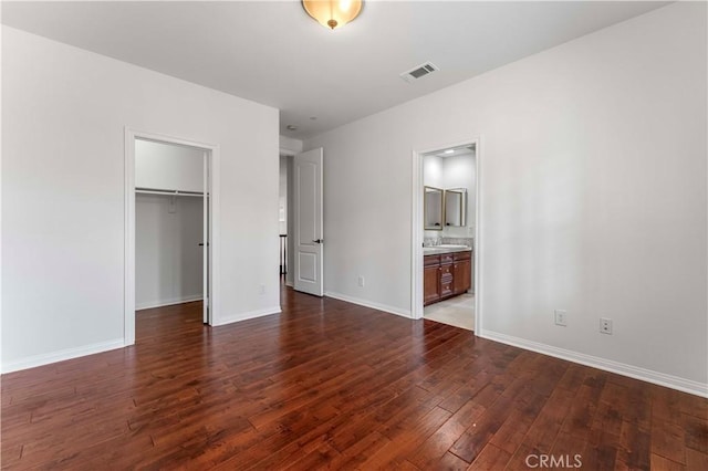 unfurnished bedroom featuring visible vents, a spacious closet, wood finished floors, and baseboards