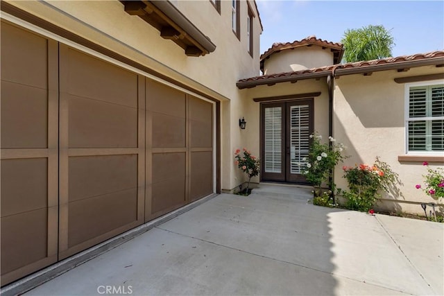 doorway to property with french doors, concrete driveway, stucco siding, and a tile roof