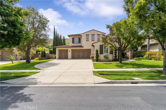 mediterranean / spanish home with a front lawn, a tiled roof, concrete driveway, an attached garage, and stucco siding