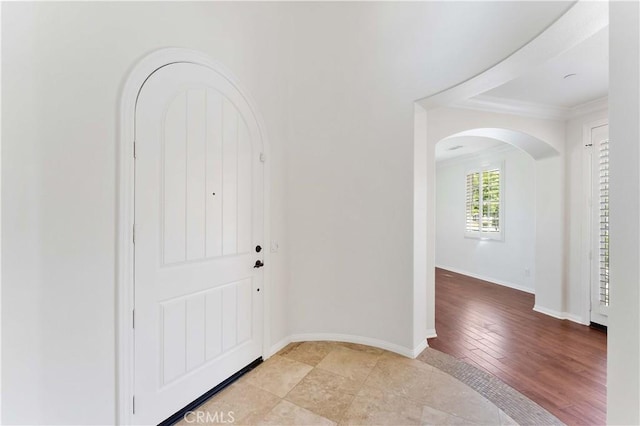 foyer entrance with arched walkways, crown molding, baseboards, and light wood-type flooring