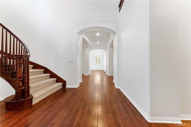 hallway with arched walkways, baseboards, stairway, and hardwood / wood-style flooring