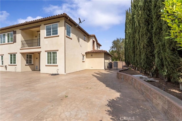 rear view of house featuring a patio, a balcony, stucco siding, and a tiled roof
