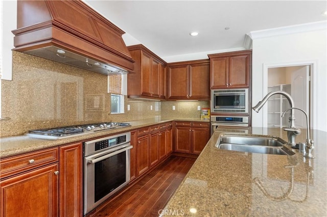 kitchen with a sink, appliances with stainless steel finishes, premium range hood, dark wood finished floors, and light stone counters