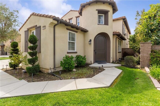 mediterranean / spanish-style house with a tiled roof, a front yard, and stucco siding