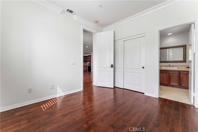 unfurnished bedroom with a sink, baseboards, visible vents, wood finished floors, and crown molding