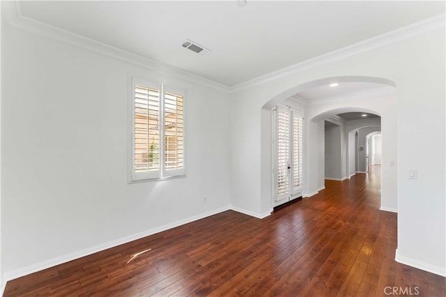 spare room featuring arched walkways, ornamental molding, visible vents, baseboards, and hardwood / wood-style flooring