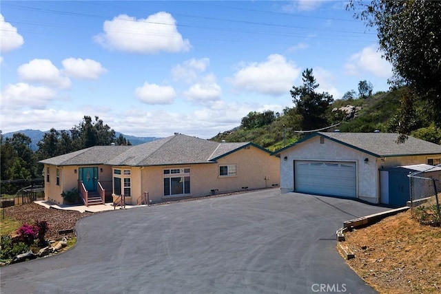 ranch-style home with a garage, aphalt driveway, stucco siding, and fence
