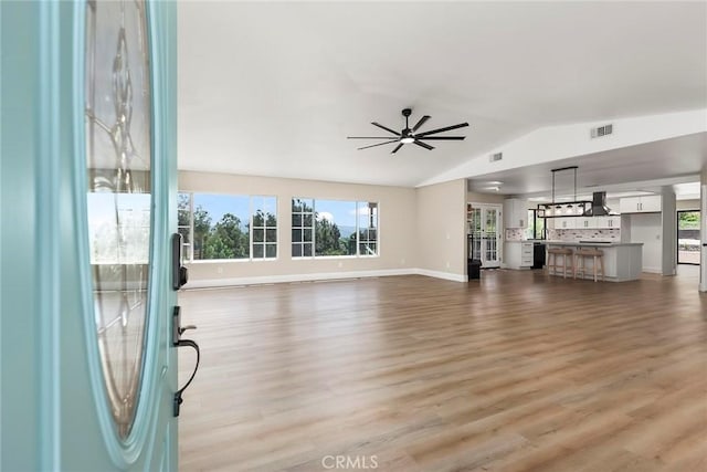 unfurnished living room with a ceiling fan, vaulted ceiling, visible vents, wood finished floors, and baseboards