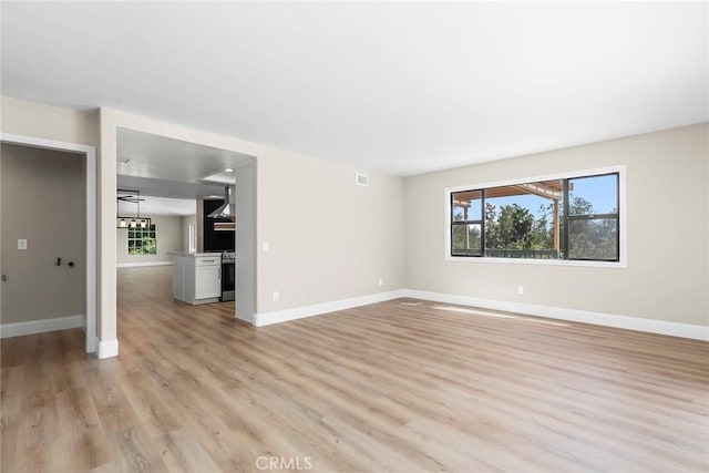 unfurnished living room featuring baseboards, light wood finished floors, and a healthy amount of sunlight